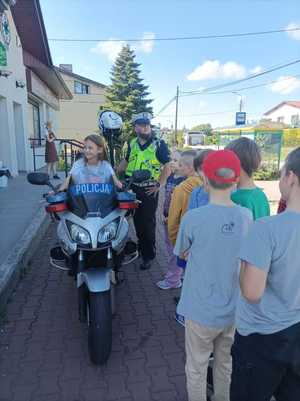 Zdjęcie przedstawiające dziewczynkę na motocyklu oraz  policjanta oraz inne dzieci.