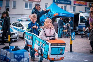 Zdjęcie przedstawiające policjanta oraz dzieci bawiące się pluszowymi pojazdami.