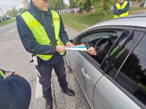 Zdjęcie przedstawiające policjanta ruchu drogowego wręczającego odblaski.