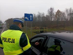 Zdjęcie przedstawiające policjanta rozmawiającegoz kierowcą znajdującym się w samochodzie.