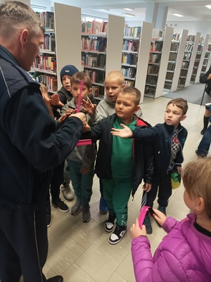 Zdjęcie przedstawiające policjanta ruchu drogowego wręczającego odblaski dzieciom.