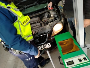 Zdjęcie przedstawiające policjanta oraz urządzenie do badania oświetlenia pojazdu..