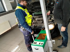 Zdjęcie przedstawiające policjanta, Pana Diagnostę oraz urządzenie do badania oświetlenia pojazdu.