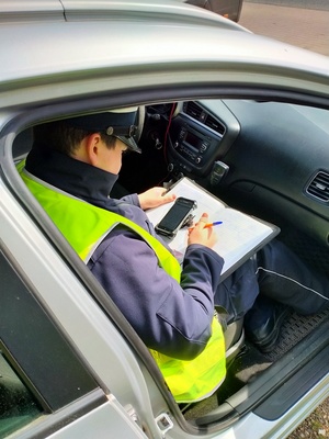 Zdjęcie przedstawiające policjanta ruchu drogowego wykonującego w trakcie wykonywania sprawdzenia danych osobowych kierowcy.