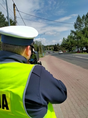 Zdjęcie przedstawiające policjanta ruchu drogowego wykonującego pomiar prędkości.