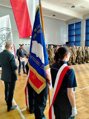 Zdjęcie przedstawiające Sztandar Szkolny trzymany przez uczniów z klasy policyjnej.