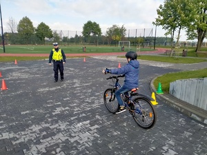 Zdjęcie przedstawiające policjanta oraz ucznia, który lewą ręką sygnalizuje manewr skrętu w lewo.