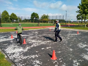 Zdjęcie przedstawiające policjanta oraz ucznia, który pokonuje slalon na rowerze.