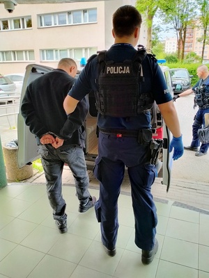 Zdjęcie policjanta oraz osoby zatrzymanej, w tle radiowóz.