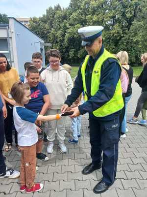 Zdjęcie przedstawiające policjanta w trakcie wręczania dziewczynce odblasku.