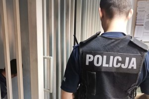 Na zdjęciu widać policjanta a obok pomieszczenie dla zatrzymanych.