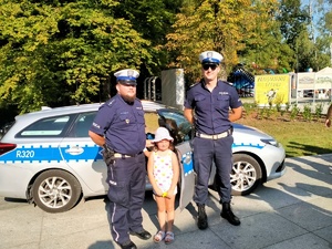 Zdjęcie przedstawiające policjantów, dziewczynki oraz radiowozu.