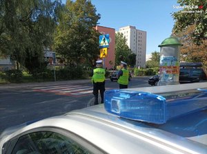 Zdjęcie przedstawiające policjantów oraz radiowóz przy przejściu dla pieszych.