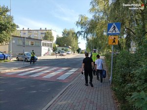 Zdjęcie przedstawiające policjantów, radiowóz oraz dzieci na przejściu.