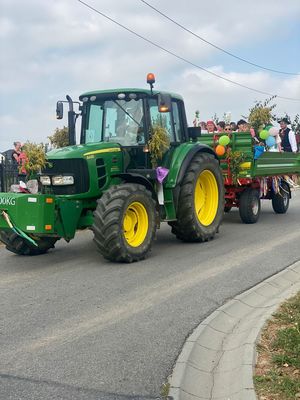 Zdjęcie przedstawiające traktor ciągnący przyczepę z uczestnikami dożynek.