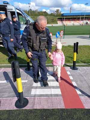 Zdjęcie przedstawiające dziecko które wraz z policjantem przechodzi po przejściu dla pieszych.