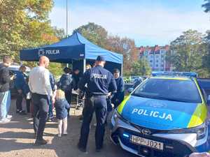 Zdjęcie przedstawiające policjanta, radiowóz oraz zebranych uczestników.