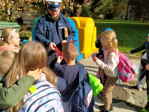 Zdjęcie policjanta rozdającego odblaski dzieciom.