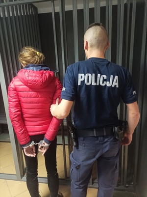 Zdjęcie kobiety z założonymi kajdankami oraz policjanta.