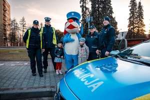 Zdjęcie przedstawiające policjantów oraz Sznupka i dzieci przy radiowozie.