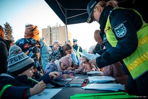 Zdjęcie przedstawiające dzieci oraz policjantkę przy stoisku profilaktycznym.