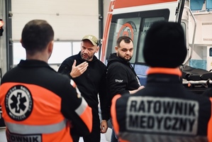 Zdjęcie 4 mężczyzn oraz samochód pogotowia ratunkowego.