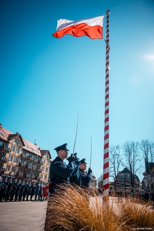 Zdjęcie przedstawiające poczt sztandarowy przy maszcie z flagą.