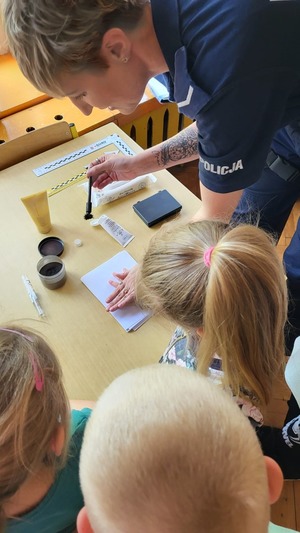 Zdjęcie przedstawiające Policjantkę w trakcie pokazywania, jak pobiera się odciski linii papilarnych.