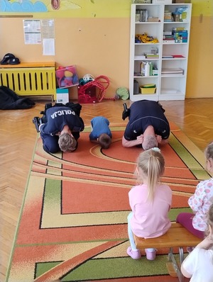 Zdjęcie przedstawiające Policjantów i przedszkolaka w trakcie pokazywania pozycji &quot;na żółwia&quot;.