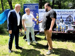 Zdjęcie przedstawiające 3 mężczyzn, w trakcie wręczania pucharu.