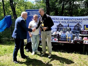 Zdjęcie przedstawiające 3 mężczyzn, w trakcie wręczania pucharu.
