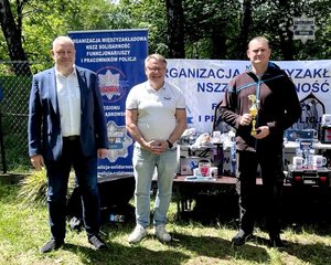 Zdjęcie przedstawiające 3 mężczyzn, w trakcie wręczania pucharu.