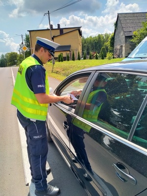 Zdjęcie przedstawiające policjanta kontrolującego samochód.