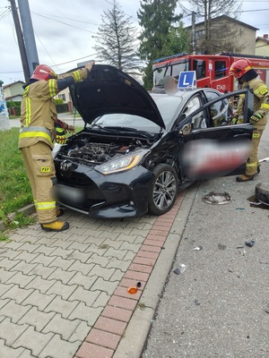 Zdjęcie przedstawiające uszkodzony samochód oraz strażaków i wóz strażacki.