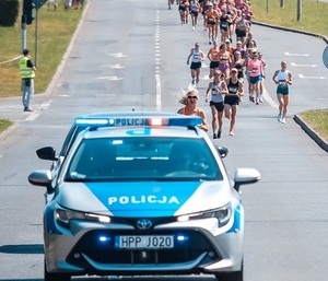 Zdjęcie przedstawiające radiowóz policyjny oraz biegaczy.