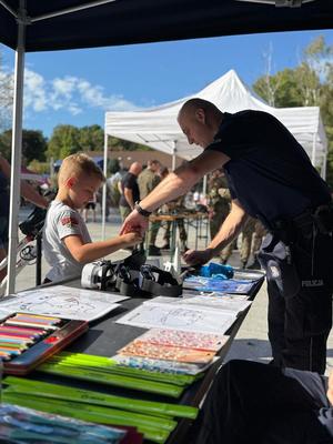 Zdjęcie przedstawiające policjanta oraz chłopca przy stoisku profilaktycznym.