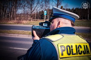 Zdjęcie policjanta trzymającego urządzenie do pomiaru prędkości.