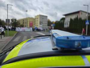 Zdjęcie przedstawiające radiowóz oraz osoby protestujące.