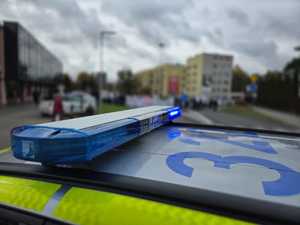 Zdjęcie przedstawiające radiowóz oraz osoby protestujące.