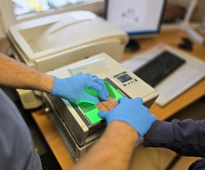 Zdjęcie mężczyzny, które policjant pobiera odciski linii papilarnych.