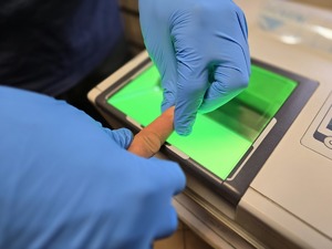 Zdjęcie mężczyzny, które policjant pobiera odciski linii papilarnych.