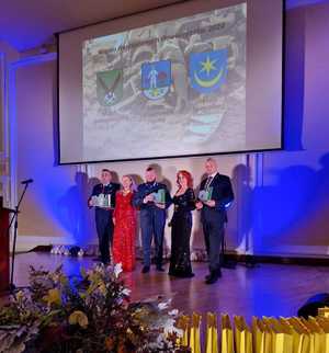 Zdjęcie przedstawiające 2 osoby prowadzące uroczystości oraz 3 osoby trzymające statuetki.