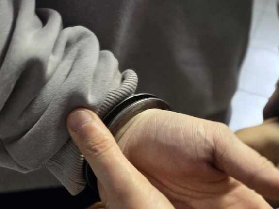 Zdjęcie dłoni policjanta oraz osoby zatrzymanej z kajdankami.