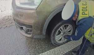 Zdjęcie policjanta ruchu drogowego wymieniającego koło w pojeździe.