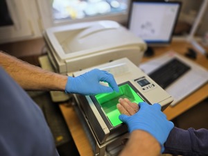 Zdjęcie policjanta oraz osoby zatrzymanej w momencie pobierania odcisków linii papilarnych.