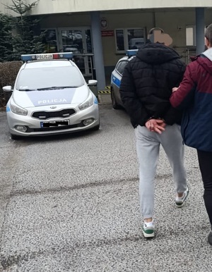 Zdjęcie przedstawiające zatrzymanego mężczyznę oraz budynek komendy oraz radiowóz policyjny.