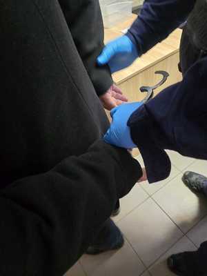 Zdjęcie osoby zatrzymanej, której policjant zakłada kajdanki.