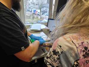 Zdjęcie kobiety zatrzymanej oraz policjanta, w trakcie pobierania odcisków linii papilarnych.