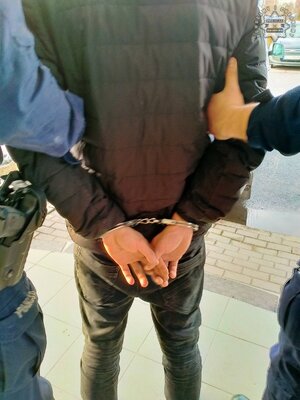 Policjanci oraz osoba zatrzymana z założonymi kajdankami.