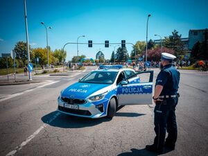 Radiowóz policyjny oraz policjant podczas zabezpieczenia biegu oraz uczestnicy.